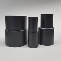 alt="line up of 6 round black resin display plinths in stacks of 2 against a white background"