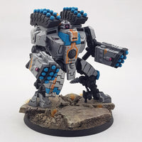 alt="tau broadside battlesuit painted in a grey and blue scheme with missile arms and racks"